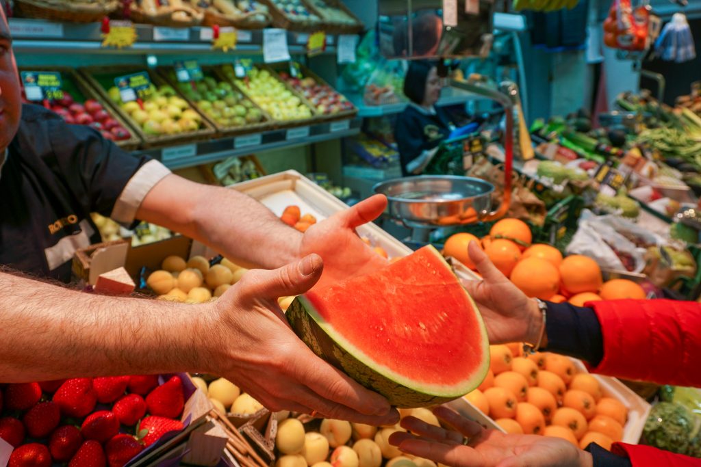 Un comerciante del mercado de Santa María de la Cabeza ofrece una porción de sandía recién cortada una clienta.